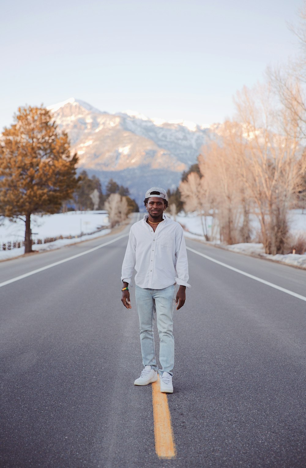 Hombre con camisa de vestir blanca y pantalones grises de pie en la carretera de asfalto gris durante el día