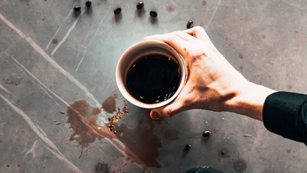 person holding white ceramic mug with black liquid