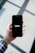 A hand holding a smartphone displaying the Uber logo on its screen. The background appears softly blurred, providing a contrast to the sharp focus on the phone. The hand is wearing a long-sleeved, checkered shirt.