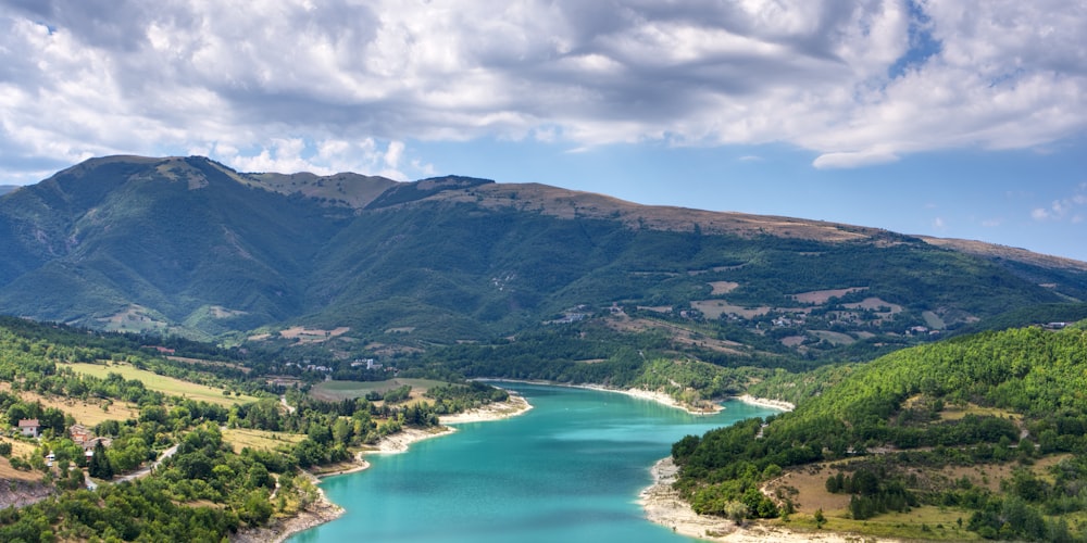 green mountains near body of water under white clouds during daytime