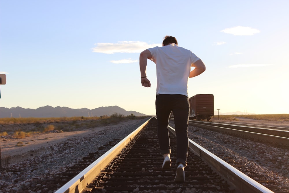 man in white t-shirt and black pants standing on train rail during daytime