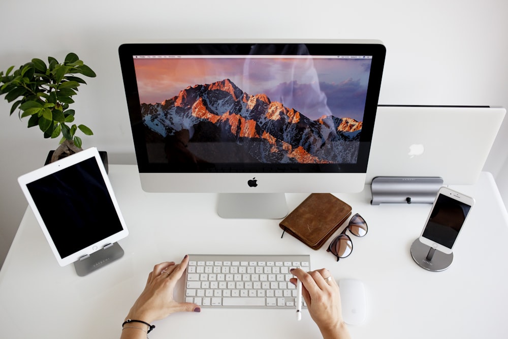 person using silver imac and apple magic keyboard