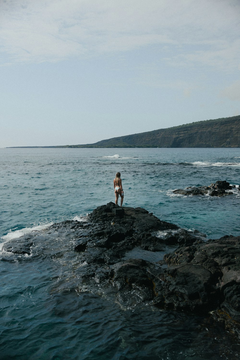 woman in white tank top and black shorts standing on rocky shore during daytime