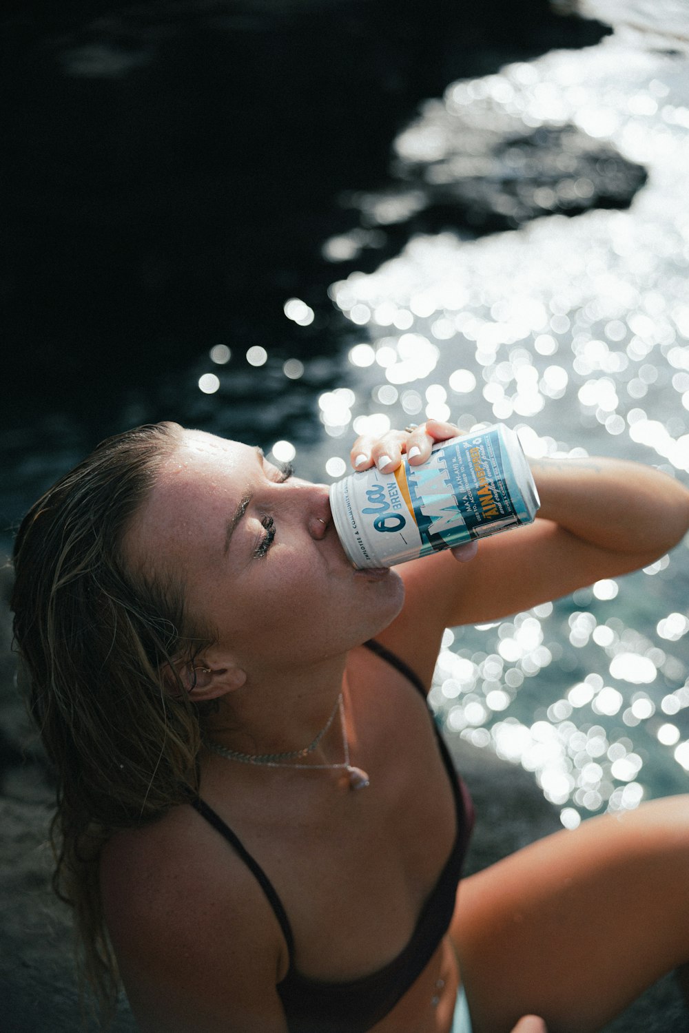 woman in blue bikini drinking from white and blue labeled can