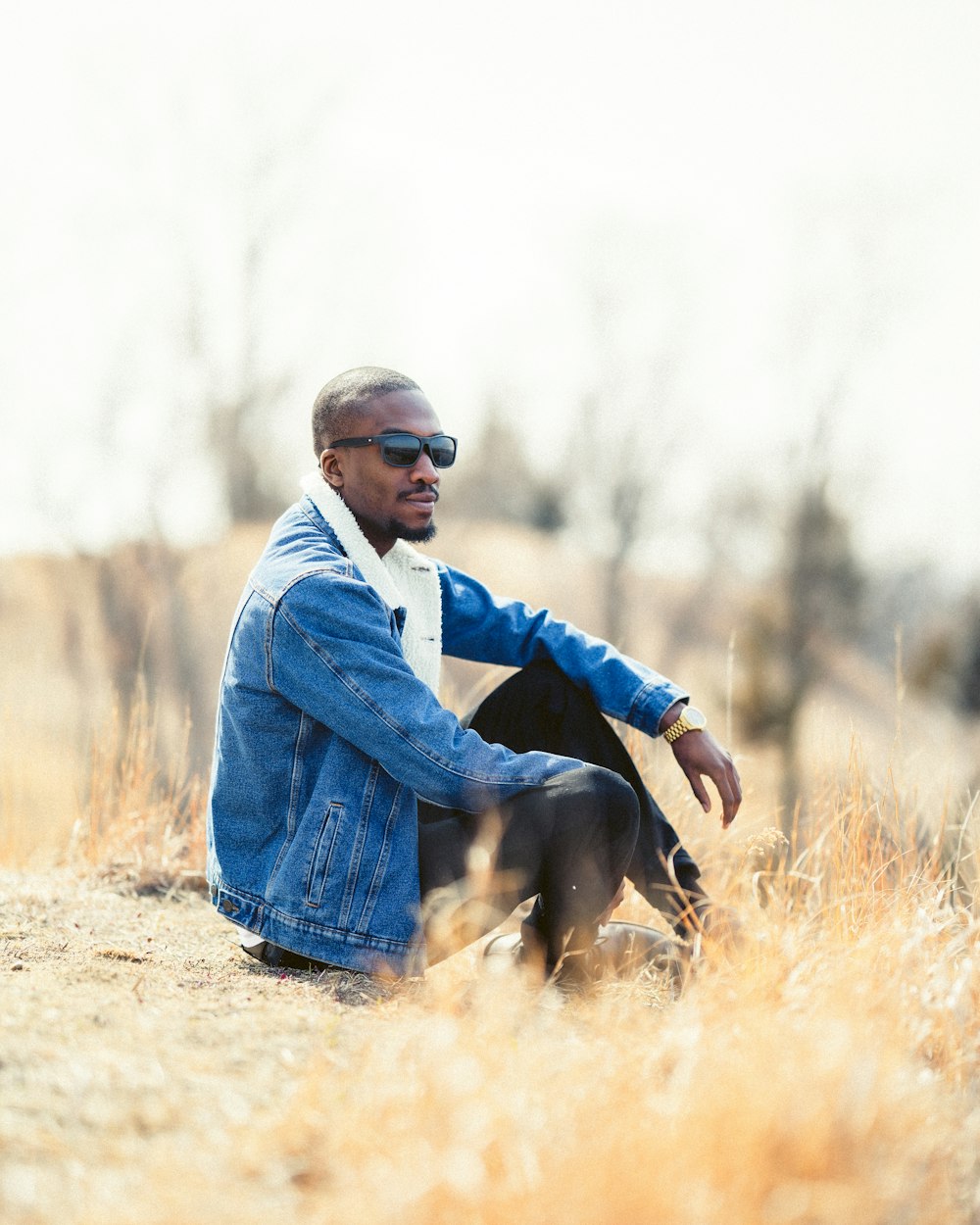 man in blue jacket and black pants sitting on brown grass field during daytime