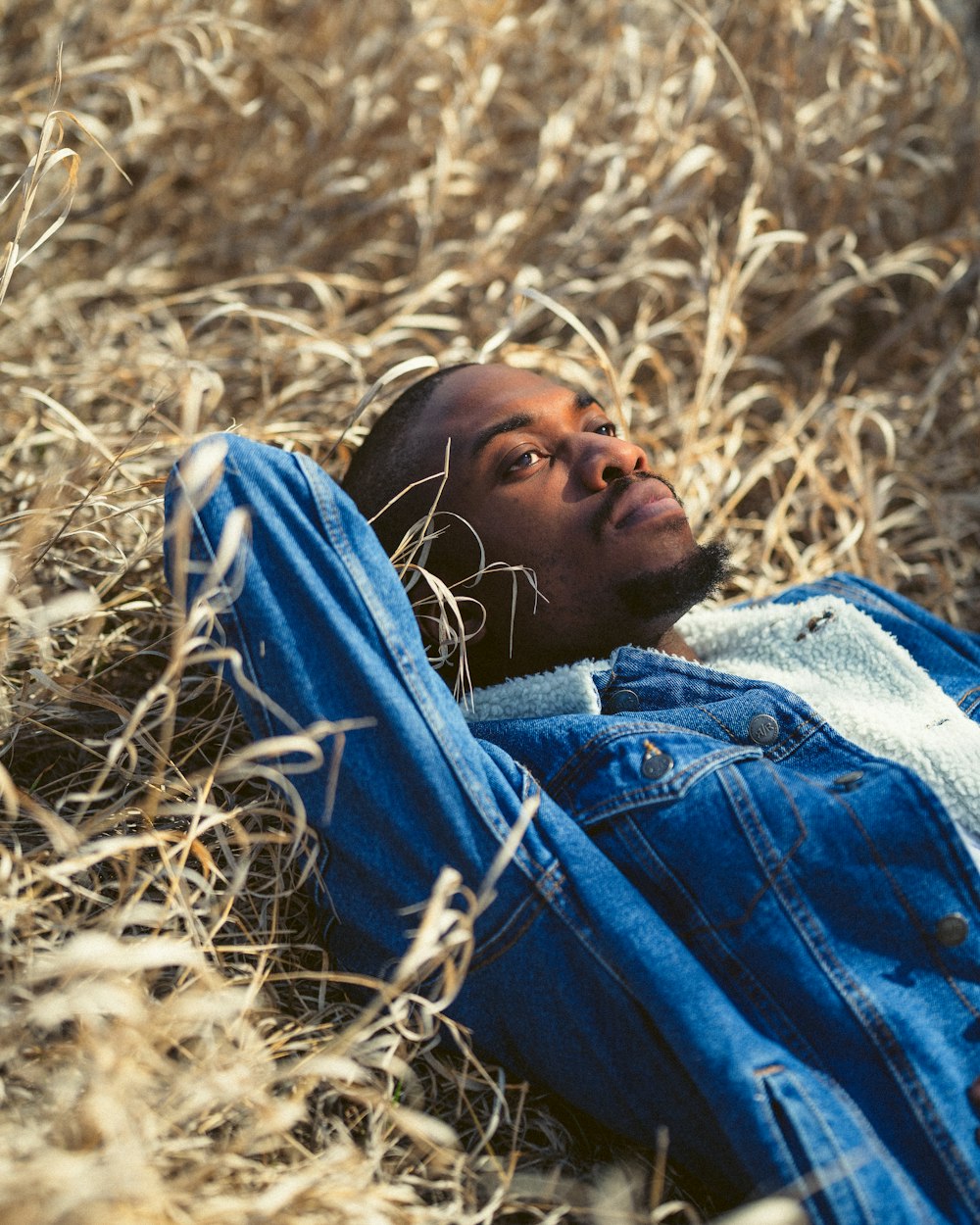 낮 동안 갈색 잔디밭에 누워 있는 파란색 데님 재킷을 입은 남자