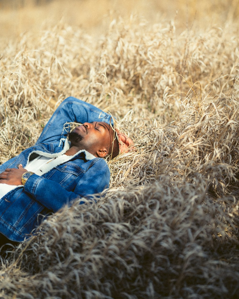 Hombre en chaqueta de mezclilla azul acostado en el campo de hierba marrón durante el día