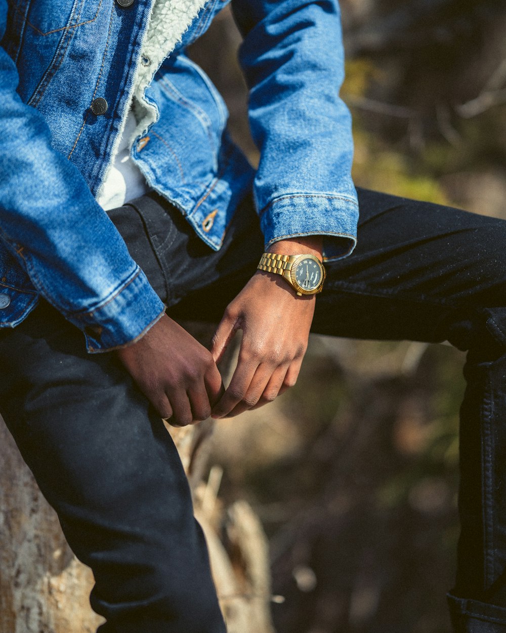 person in blue denim jacket and black pants sitting on brown rock