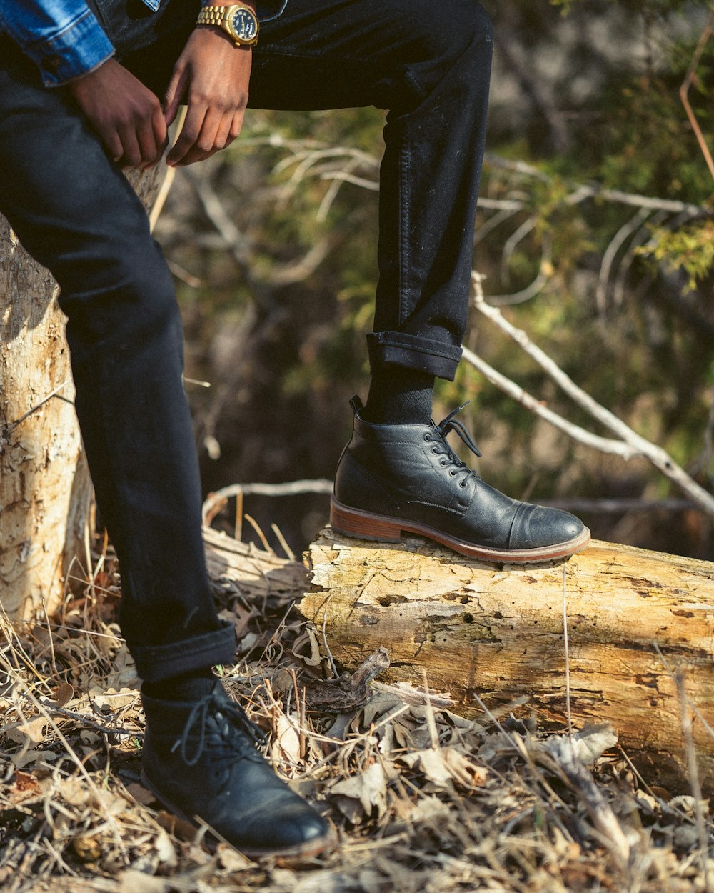 Persona con pantalones negros y botas de cuero negras de pie sobre un tronco de madera marrón