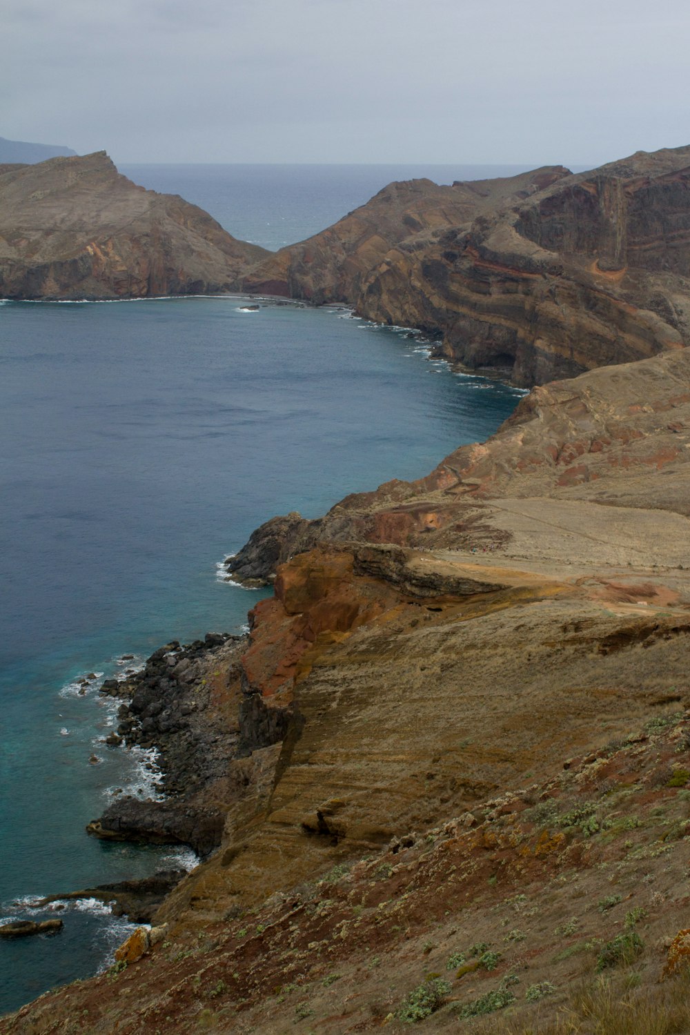 brown and green mountain beside blue sea during daytime