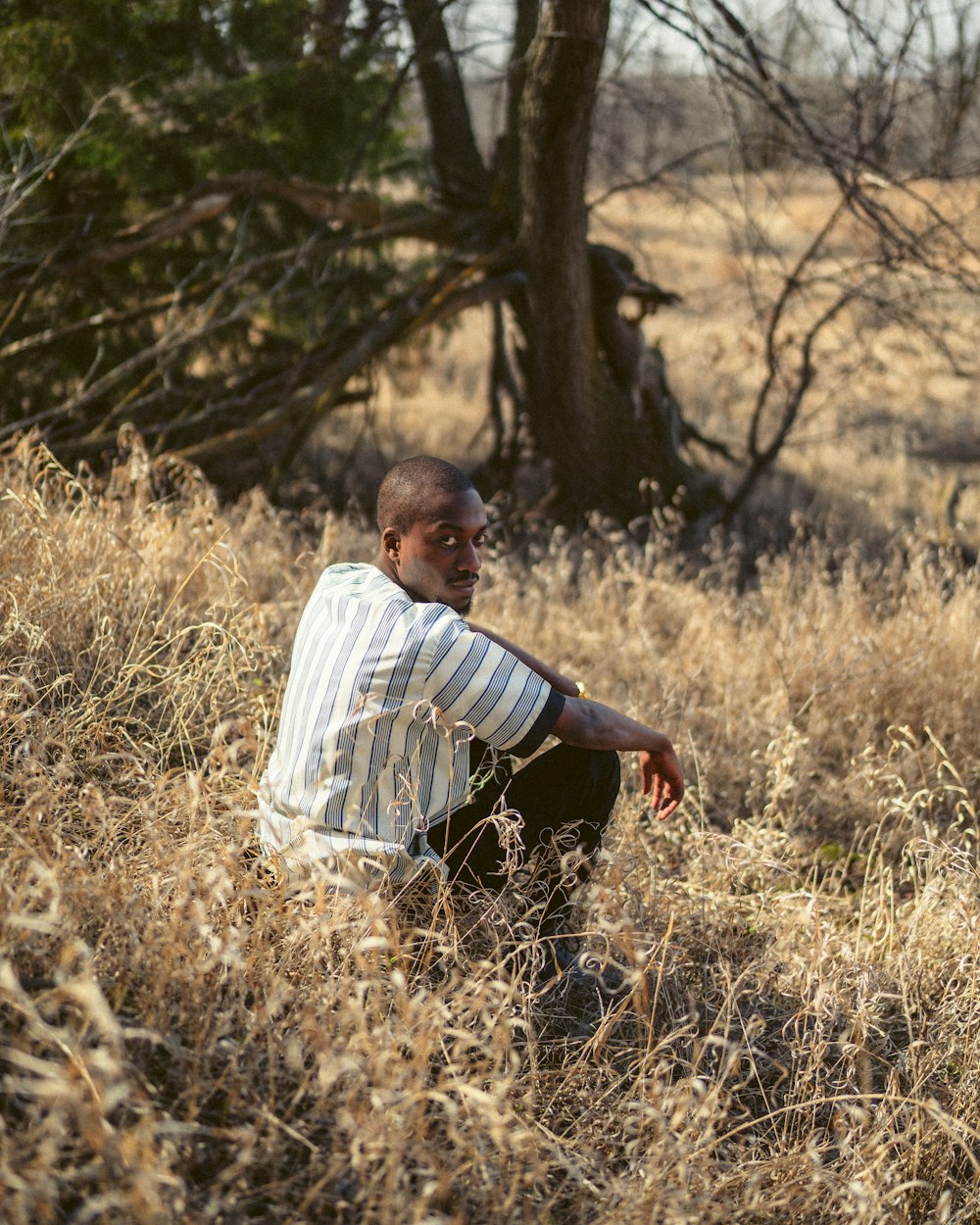 man in white and black stripe dress shirt sitting on brown grass field during daytime