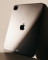 The image features the back of a sleek metallic tablet, prominently displaying the logo of a major technology brand. Soft lighting creates a play of shadows on the surface, enhancing its modern and sophisticated design.