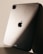 The image features the back of a sleek metallic tablet, prominently displaying the logo of a major technology brand. Soft lighting creates a play of shadows on the surface, enhancing its modern and sophisticated design.
