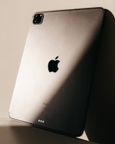 The image features the back of a sleek metallic tablet, prominently displaying the logo of a major technology brand. Soft lighting creates a play of shadows on the surface, enhancing its modern and sophisticated design.