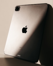 The image features the back of a sleek metallic tablet, prominently displaying the logo of a major technology brand. Soft lighting creates a play of shadows on the surface, enhancing its modern and sophisticated design.