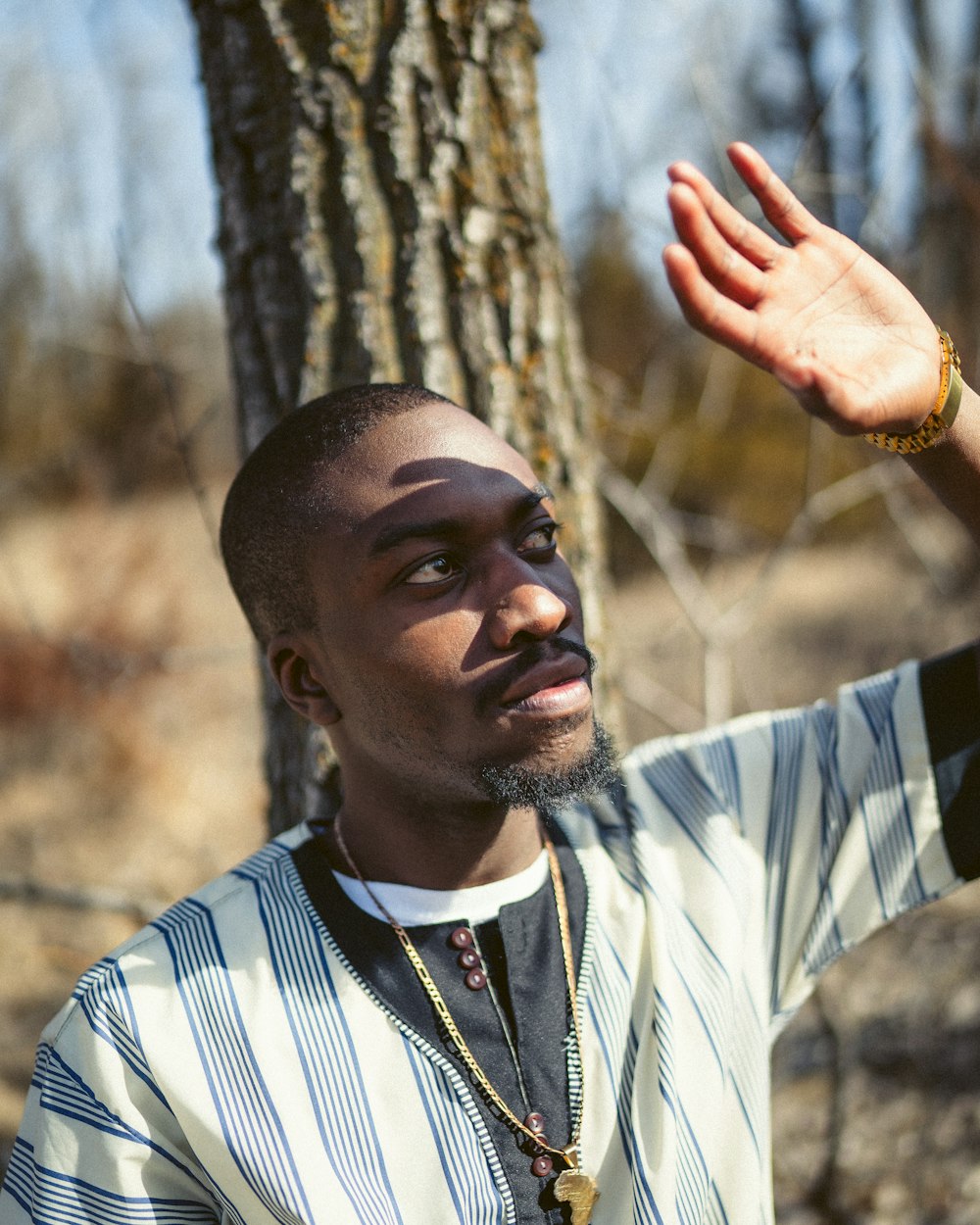 man in white and black striped polo shirt holding brown tree branch during daytime