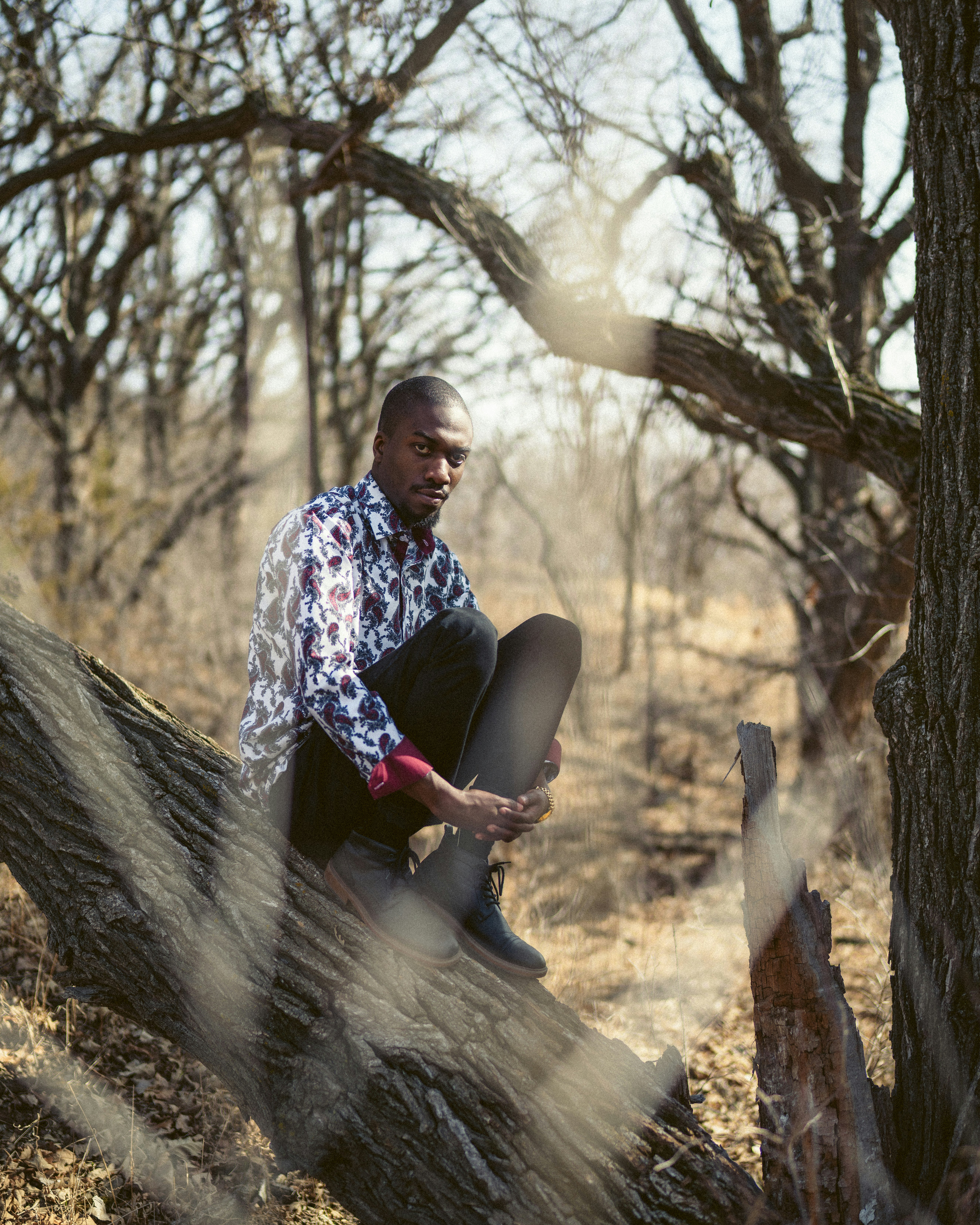 man in black and white floral shirt sitting on tree log during daytime