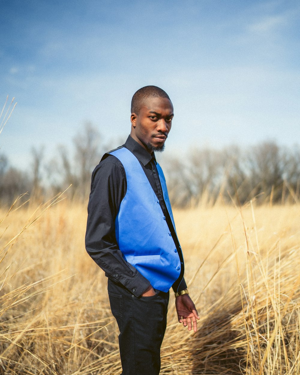 uomo in gilet nero e camicia blu in piedi sul campo di erba marrone durante il giorno