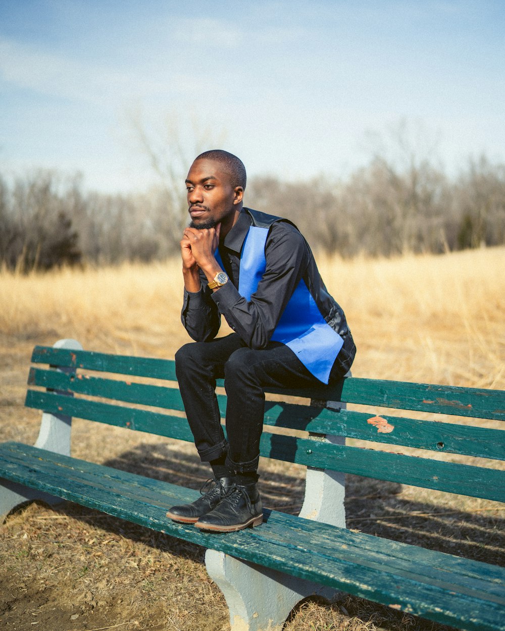 Hombre en chaqueta azul sentado en banco de madera marrón durante el día
