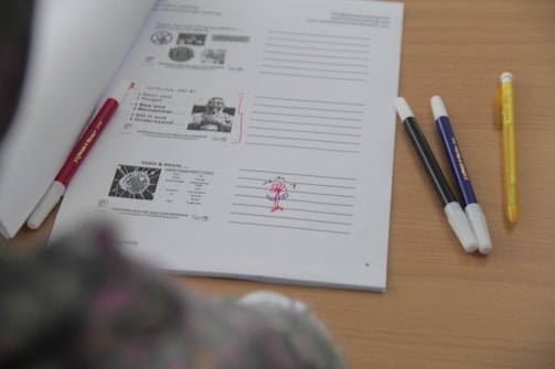 A table with a sheet of paper containing text and diagrams, organized with lined spaces for notes. Several pens of different colors are placed next to the sheet.
