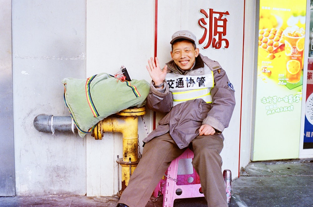 man in green jacket and brown pants sitting on red plastic chair