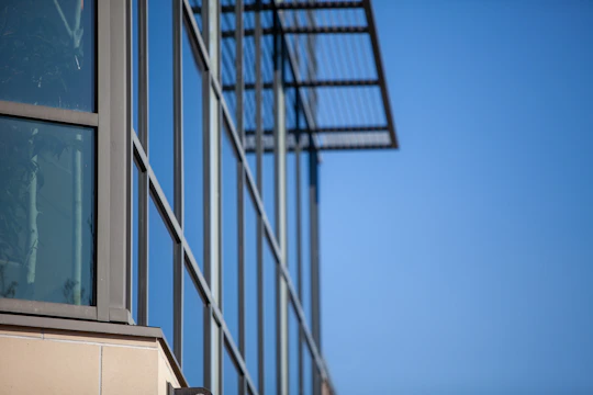 A sleek modern glass facade with aluminum frames reflecting a clear blue sky.