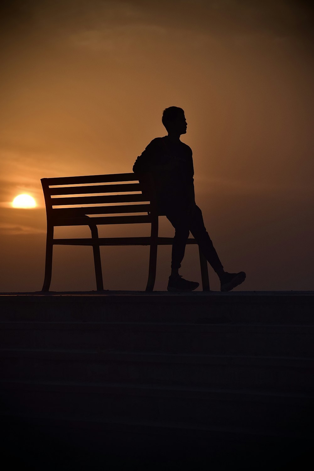 silhouette of man standing beside bench during sunset