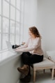 woman in white long sleeve shirt and black pants sitting on bed using laptop computer