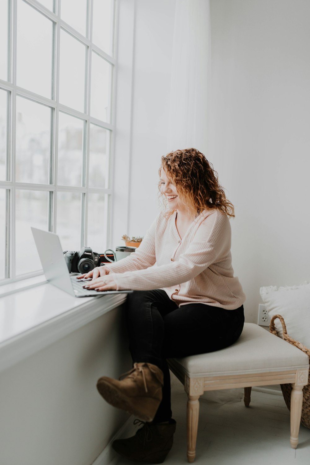 woman in white long sleeve shirt and black pants sitting on bed using laptop computer