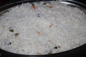 A rustic wooden bowl filled with steaming white IR64 non-basmati rice on a jute cloth.