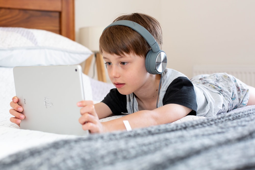 menino na camisa azul usando fones de ouvido deitado na cama