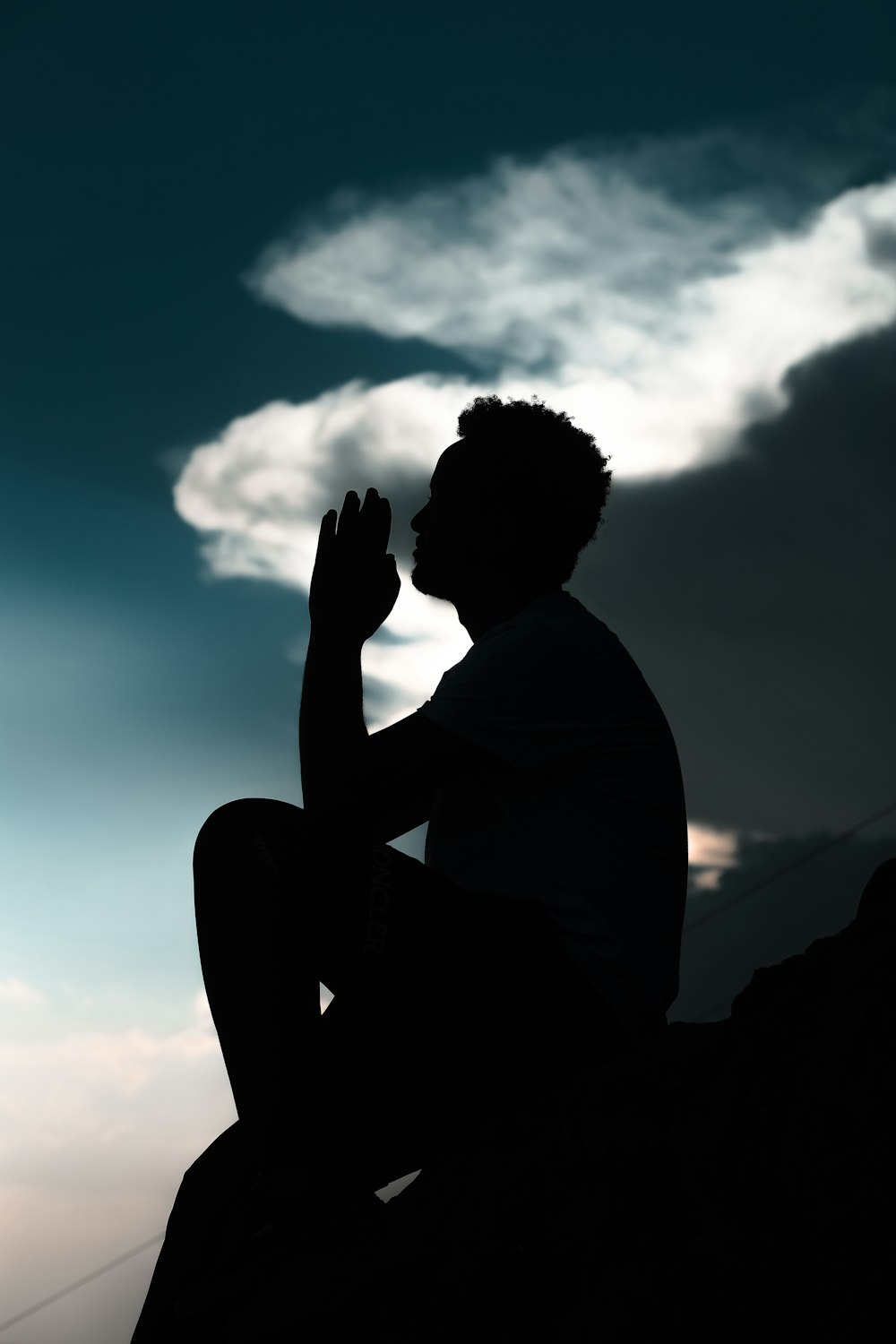 silhouette of man sitting on rock during daytime