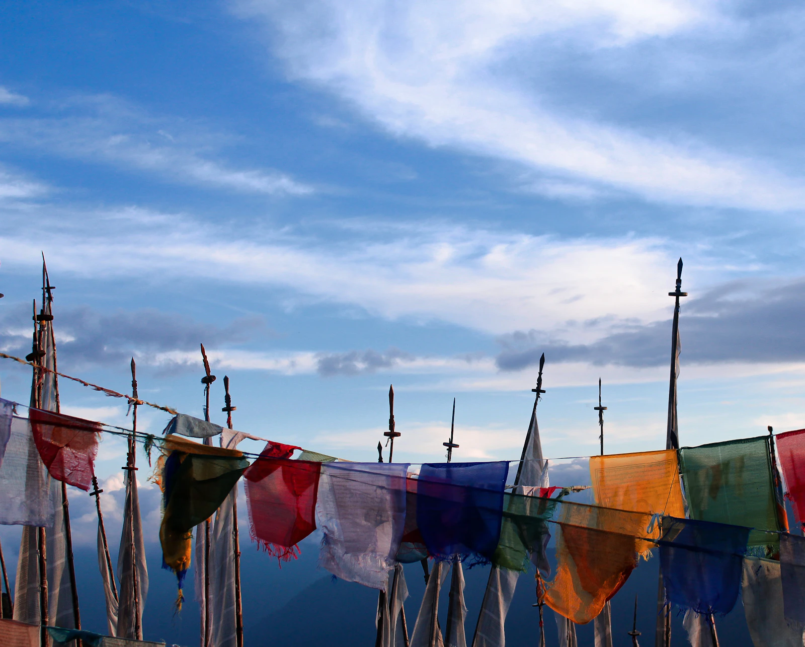 Prayer flags strung between tall poles on a high ridge in Bhutan, under blue sky and high cloud