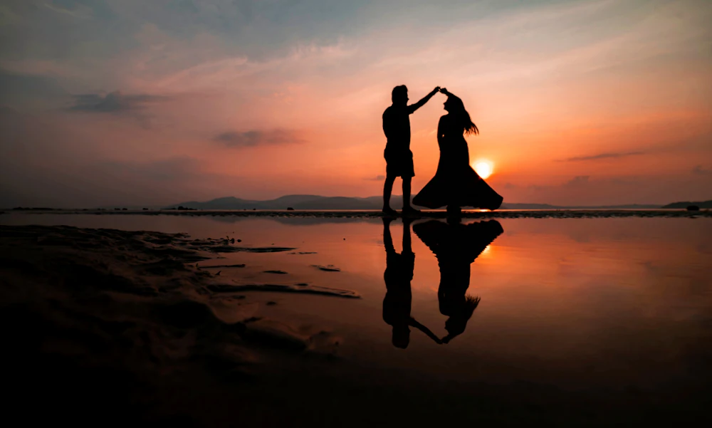 Hai người nắm tay nhau xoay tròn trên bãi biển lúc mặt trời lặn