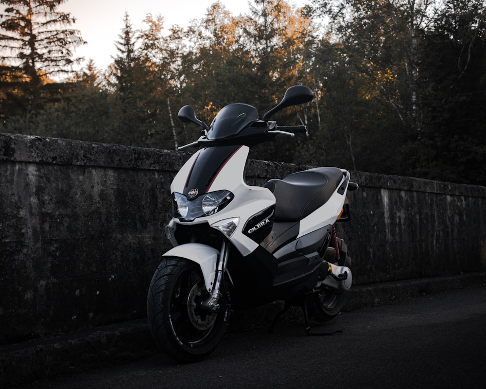 white and black motor scooter parked beside gray concrete wall during daytime