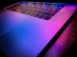 Close-up of hands typing on a laptop keyboard with glowing neon accents reflecting a modern, tech-savvy environment.
