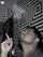 A man exhales smoke while holding a cigarette, set against a geometric black and white patterned wall. Smoke curls upwards in wisps above him. The lighting casts a dramatic effect, highlighting the patterns.