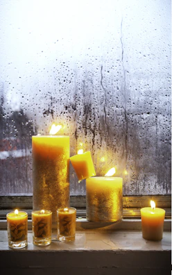 A collection of colorful candles in various shapes and sizes displayed on a sunlit windowsill.