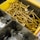 A plastic container is divided into compartments. One compartment holds a large quantity of brass-colored screws. Another compartment contains several round metallic washers.