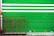 A green metal rolling shutter with two horizontal white stripes is partially visible. In front of it, there is a decorative red iron railing with intricate swirling patterns and floral motifs. The ground is concrete, and there are several small signs or stickers at the bottom of the shutter.
