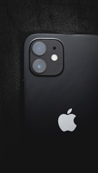 A close-up of a black smartphone with dual camera lenses and a flash on the back, featuring a prominent Apple logo in the lower section.
