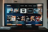 A television screen displaying the ESPN+ streaming interface with various sports-related shows and categories. The screen includes sections such as 'Browse by Shows' and 'Best of Drew Brees' with thumbnails of sports programs featuring athletes in action and analysts.