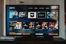 A television screen displaying the ESPN+ streaming interface with various sports-related shows and categories. The screen includes sections such as 'Browse by Shows' and 'Best of Drew Brees' with thumbnails of sports programs featuring athletes in action and analysts.