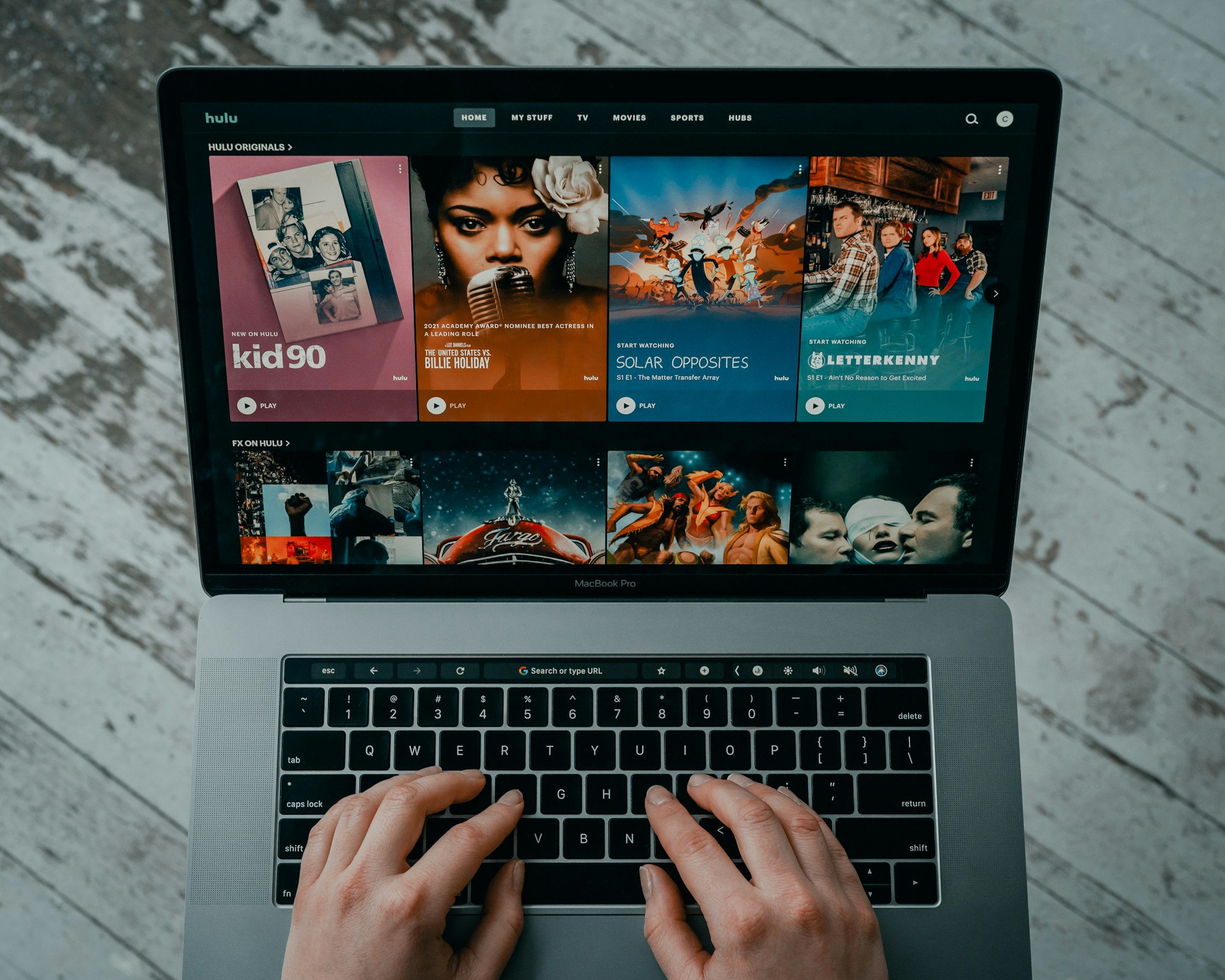 This photo shows two hands hovering over a laptop keyboard. A streaming service home page is displayed on the laptop screen.