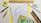 A variety of stationery items arranged on a surface, including a spiral notebook with graph paper, a wooden ruler, a protractor, a mechanical pencil, colored pencils, a yellow highlighter, a pen, an eraser, and a small box. The colors are vibrant and the items are neatly organized.