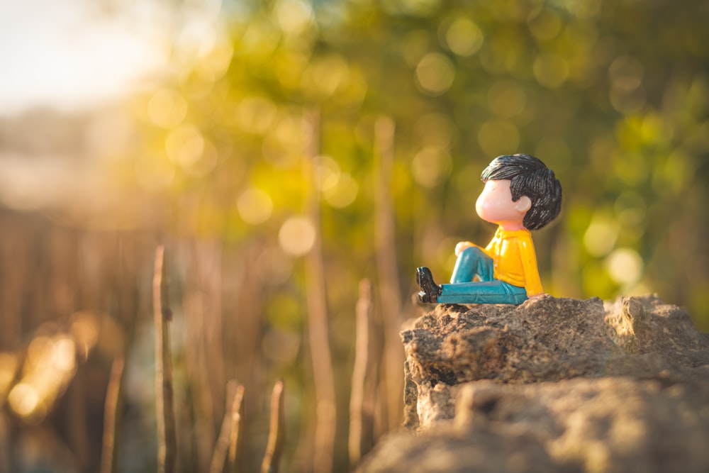 boy in yellow shirt and blue pants sitting on rock