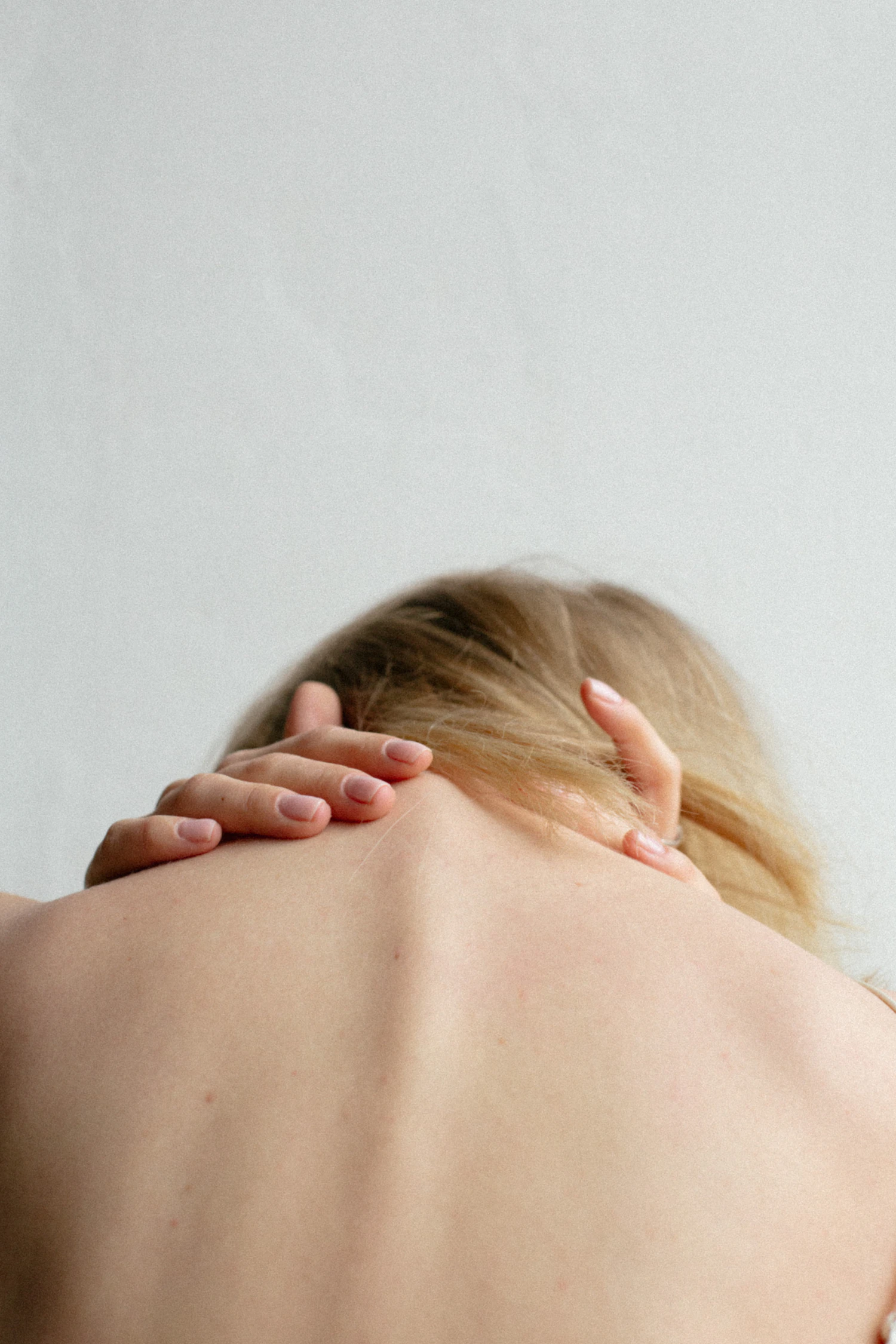 A client's hands resting at the back of her own neck, shoulders bare