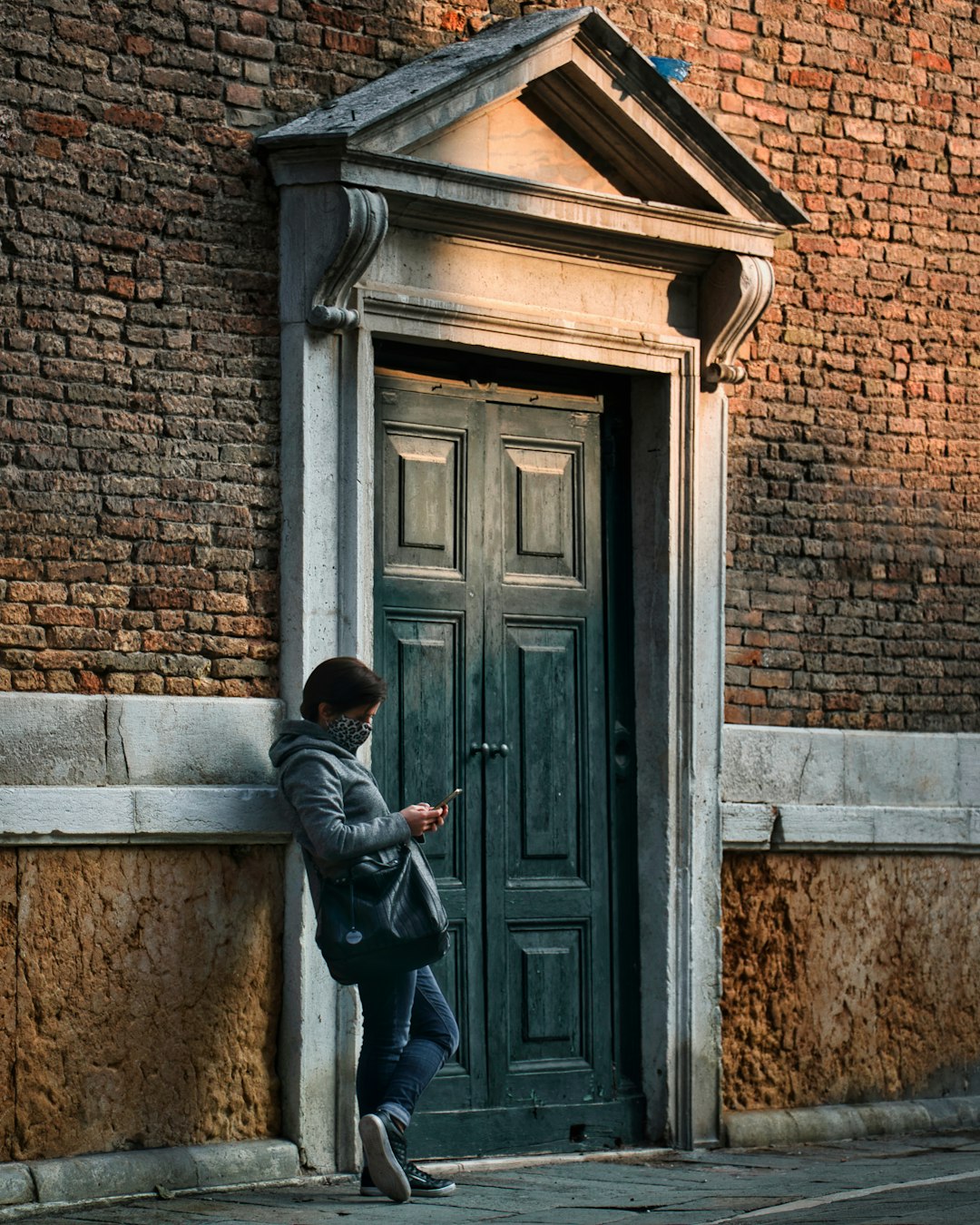 man in black jacket and black pants standing in front of brown brick building