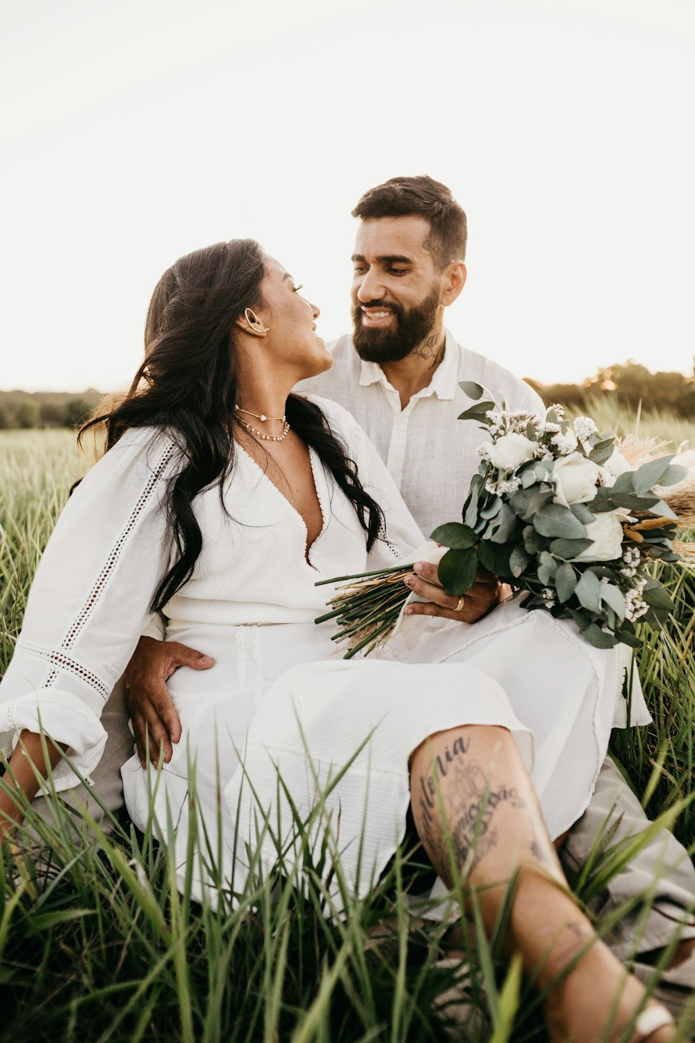 man in white suit and woman in white dress holding bouquet of flowers