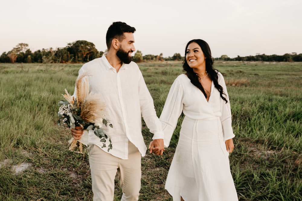 homem e mulher na camisa branca de manga comprida andando no campo de grama verde durante o dia